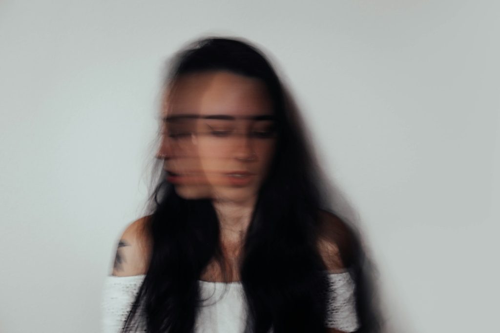 Blurred woman with double exposure effect, dark hair and white top, against plain background